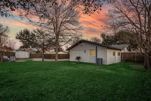 yard at dusk with an outbuilding, a fenced backyard, a patio, and a shed