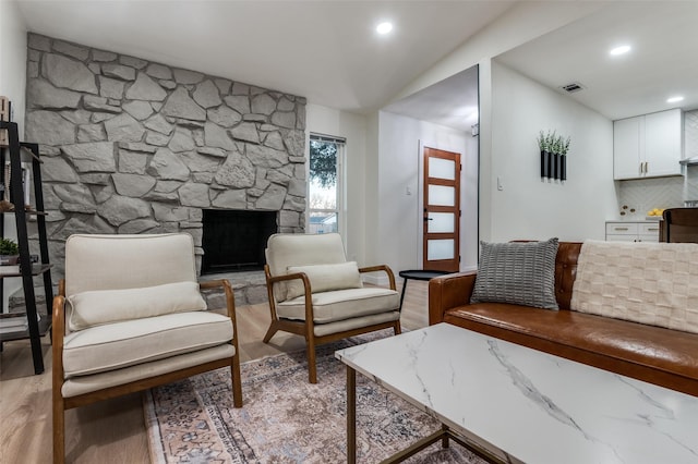 living area with light wood-style floors, recessed lighting, visible vents, and a stone fireplace