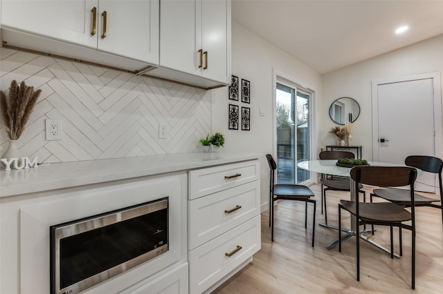 kitchen featuring tasteful backsplash, lofted ceiling, light countertops, stainless steel microwave, and light wood-style flooring