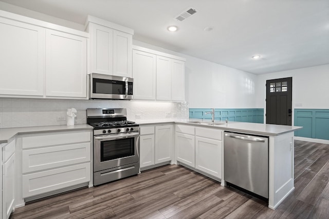 kitchen with visible vents, a sink, a peninsula, stainless steel appliances, and dark wood-style flooring