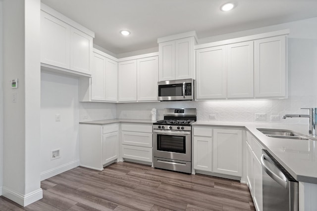 kitchen with wood finished floors, a sink, decorative backsplash, stainless steel appliances, and white cabinetry