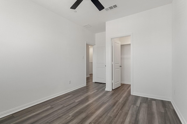 unfurnished bedroom featuring dark wood-style floors, visible vents, a spacious closet, and baseboards