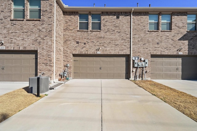 view of property with brick siding, a garage, driveway, and central AC