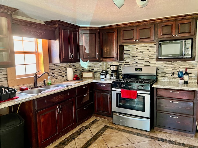 kitchen with light tile patterned floors, decorative backsplash, stainless steel range with gas stovetop, a sink, and a textured ceiling