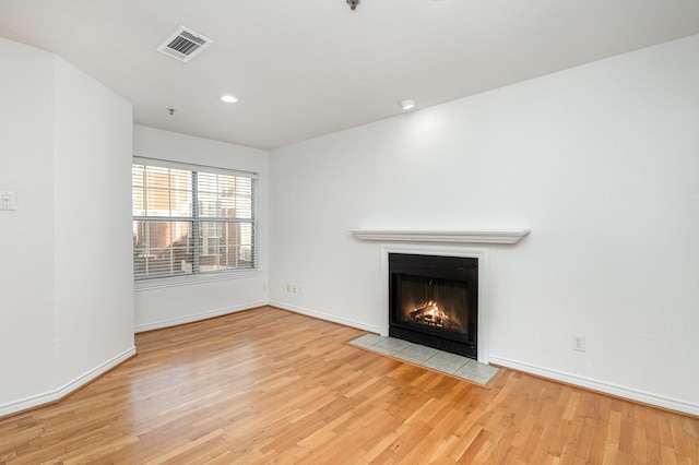 unfurnished living room featuring a fireplace with flush hearth, visible vents, baseboards, and wood finished floors