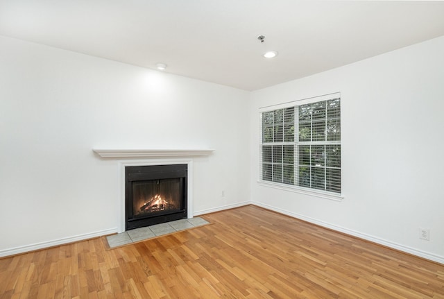 unfurnished living room with a fireplace with flush hearth, baseboards, and wood finished floors