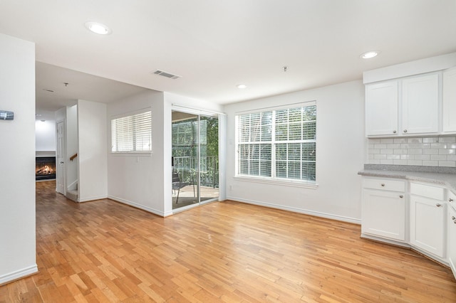 unfurnished dining area with a lit fireplace, light wood finished floors, visible vents, and baseboards