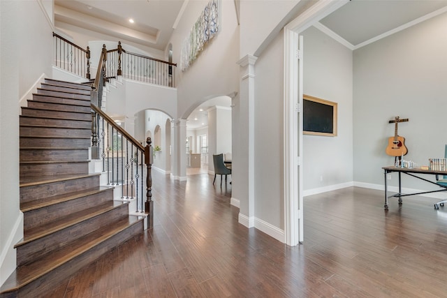 entrance foyer featuring arched walkways, wood finished floors, baseboards, stairs, and decorative columns