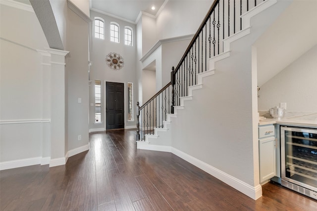 foyer entrance with wine cooler, a high ceiling, dark wood-style flooring, baseboards, and ornate columns