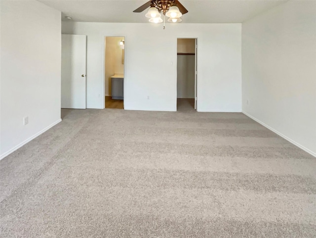 unfurnished bedroom with baseboards, ensuite bath, ceiling fan, carpet, and a walk in closet