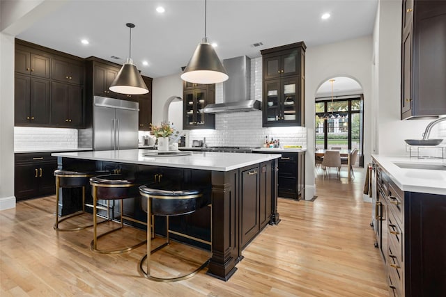 kitchen featuring wall chimney range hood, arched walkways, stainless steel built in refrigerator, and a sink