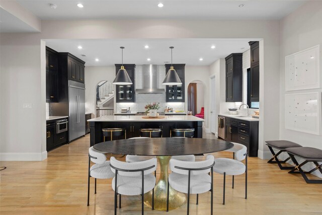 kitchen featuring arched walkways, a kitchen island, a sink, dark cabinetry, and wall chimney exhaust hood