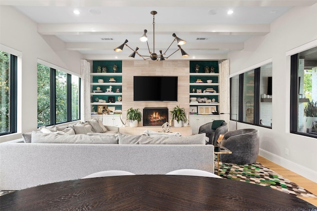 living room with built in shelves, beam ceiling, a large fireplace, a healthy amount of sunlight, and a chandelier