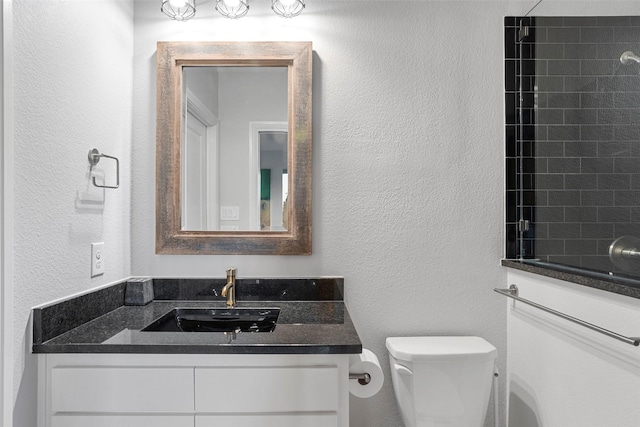 bathroom featuring toilet, a textured wall, walk in shower, and vanity