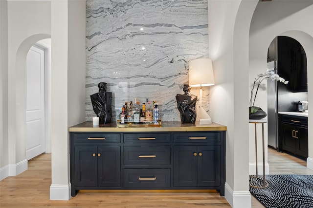 bar featuring arched walkways, light wood-style flooring, baseboards, backsplash, and a dry bar