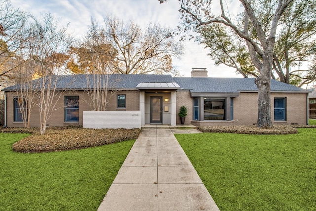 single story home featuring roof with shingles, a chimney, a front lawn, and brick siding