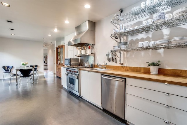 kitchen with stainless steel appliances, butcher block counters, white cabinets, concrete floors, and wall chimney exhaust hood