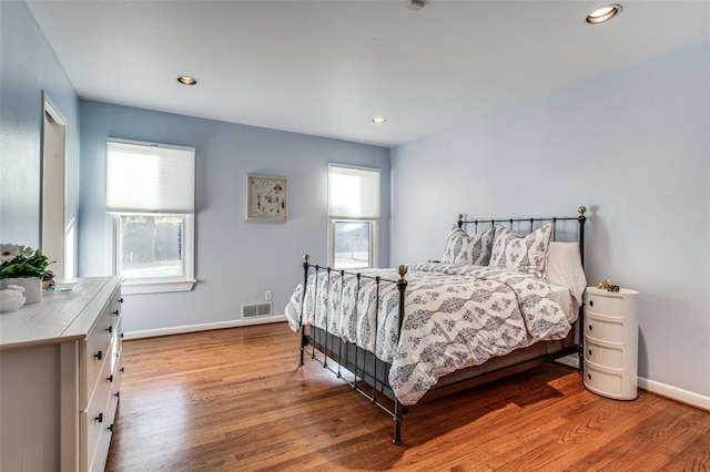 bedroom featuring baseboards, visible vents, multiple windows, and wood finished floors