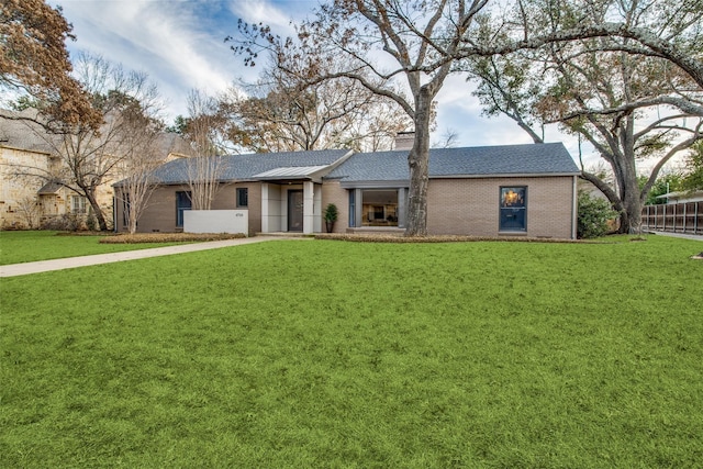 ranch-style home featuring a chimney, roof with shingles, fence, a front yard, and brick siding