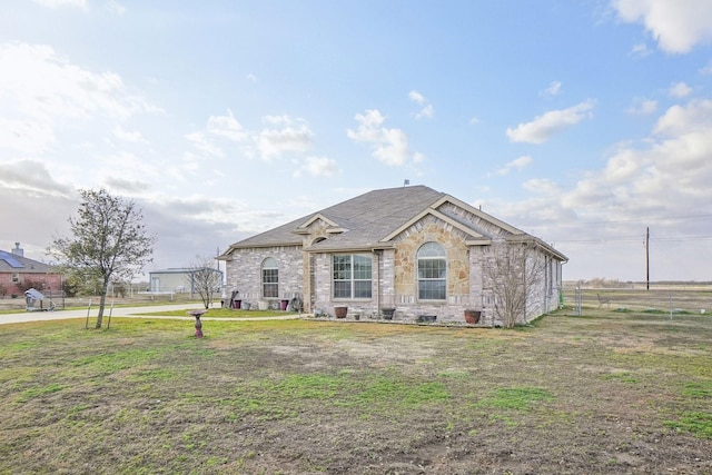 view of front of house featuring a front yard, stone siding, roof with shingles, and fence