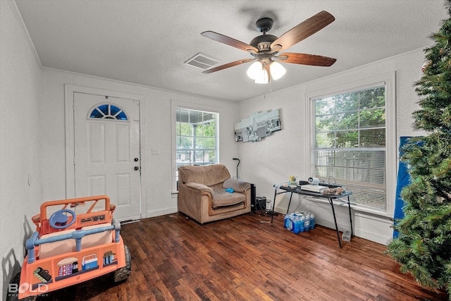 living area with visible vents, ornamental molding, wood finished floors, a textured ceiling, and a ceiling fan