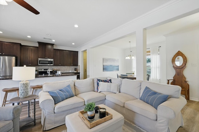 living room featuring baseboards, ceiling fan with notable chandelier, crown molding, light wood-type flooring, and recessed lighting