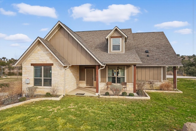 view of front of property featuring a front yard, stone siding, roof with shingles, board and batten siding, and a patio area