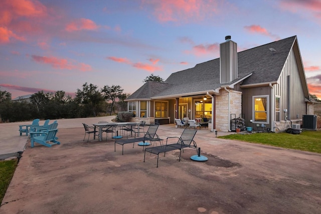 back of property at dusk with stone siding, board and batten siding, a patio area, and central air condition unit