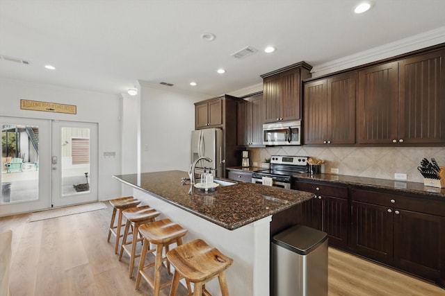 kitchen with tasteful backsplash, visible vents, a kitchen breakfast bar, a kitchen island with sink, and stainless steel appliances