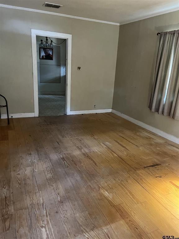 spare room featuring baseboards, wood-type flooring, visible vents, and crown molding