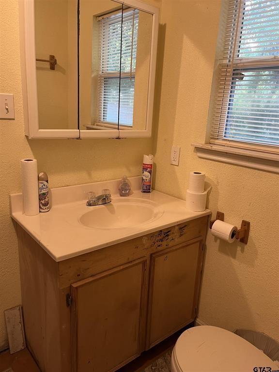 half bathroom featuring a textured wall, vanity, and toilet