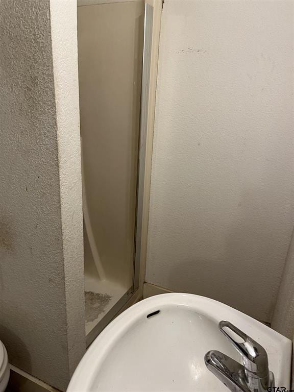 bathroom featuring toilet, a shower stall, a sink, and a textured wall