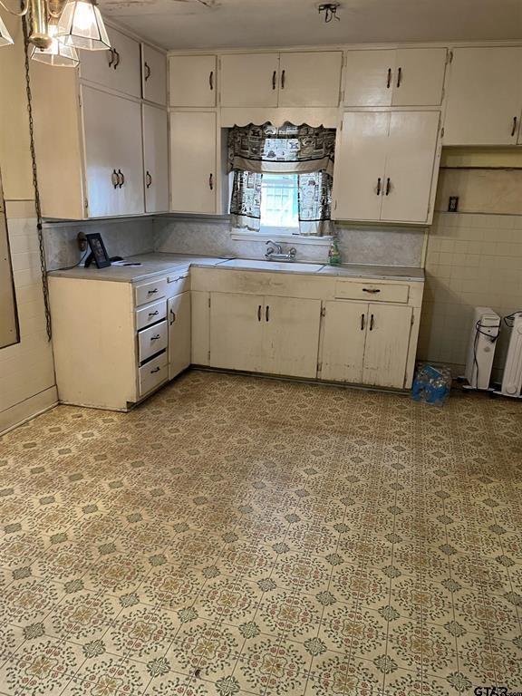 kitchen with light floors, light countertops, decorative backsplash, white cabinetry, and a sink