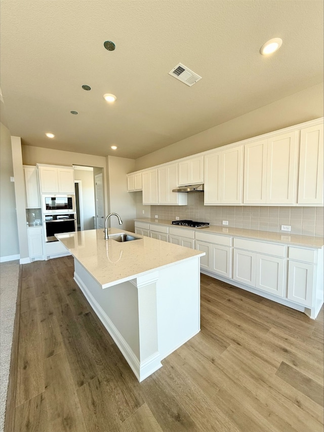 kitchen featuring visible vents, decorative backsplash, light wood-type flooring, gas cooktop, and a sink