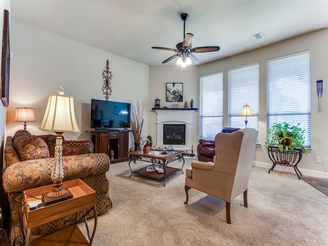 living area with a ceiling fan, a glass covered fireplace, light colored carpet, and visible vents