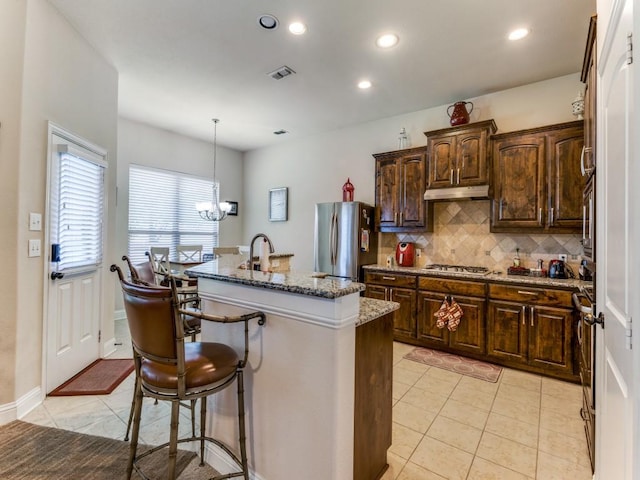 kitchen featuring a breakfast bar, visible vents, appliances with stainless steel finishes, a kitchen island with sink, and under cabinet range hood