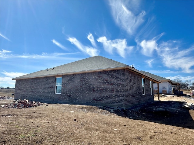 view of property exterior with brick siding and a shingled roof