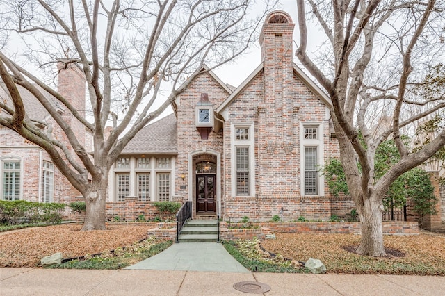 english style home with brick siding, a chimney, and a shingled roof