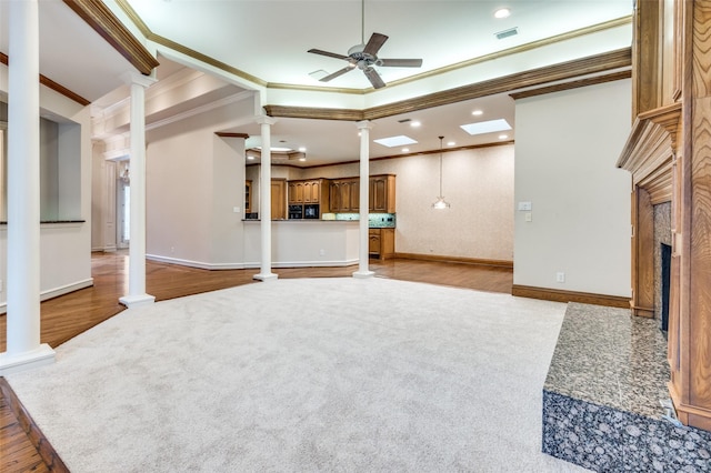 carpeted living area featuring a premium fireplace, a ceiling fan, baseboards, ornamental molding, and ornate columns