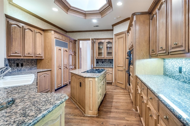 kitchen featuring a raised ceiling, crown molding, light wood-style floors, gas stovetop, and a sink