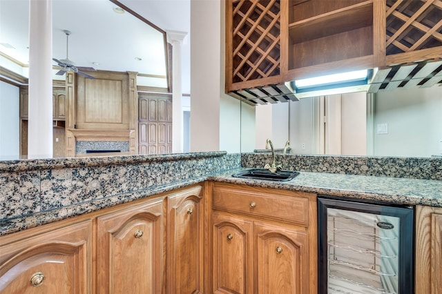 kitchen featuring ceiling fan, wine cooler, stone countertops, a sink, and decorative columns