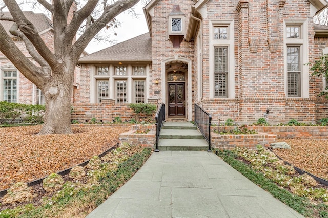 entrance to property featuring brick siding and a shingled roof