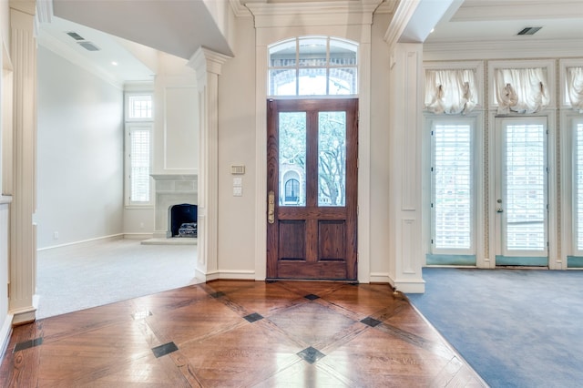 carpeted foyer entrance with a fireplace with raised hearth, a high ceiling, baseboards, ornamental molding, and ornate columns