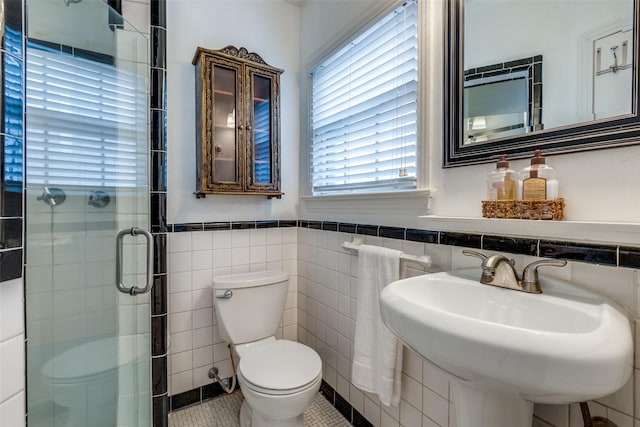 bathroom featuring a wainscoted wall, tile walls, toilet, a sink, and a shower stall