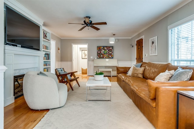 living area with light wood-type flooring, ceiling fan, a fireplace, and crown molding