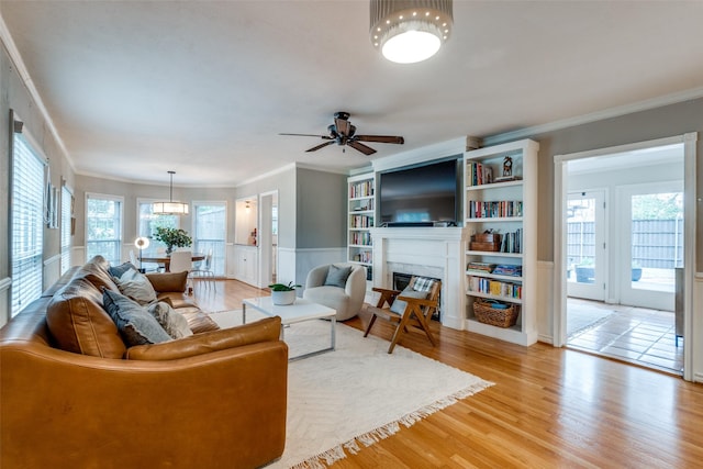 living area featuring light wood finished floors, ceiling fan, ornamental molding, and a glass covered fireplace