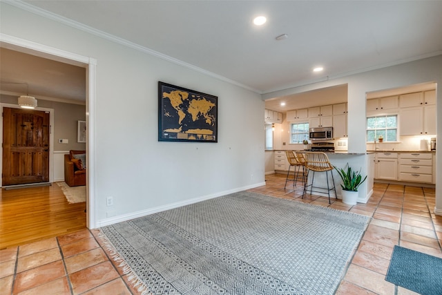 kitchen with baseboards, white cabinets, stainless steel microwave, crown molding, and a kitchen bar