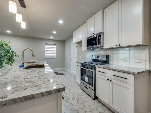 kitchen featuring light stone counters, a sink, stainless steel appliances, white cabinetry, and backsplash