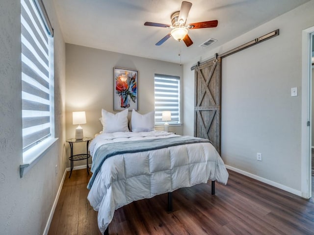 bedroom with visible vents, a barn door, a ceiling fan, wood finished floors, and baseboards