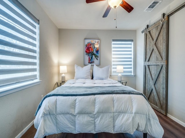 bedroom featuring a barn door, baseboards, visible vents, a ceiling fan, and wood finished floors